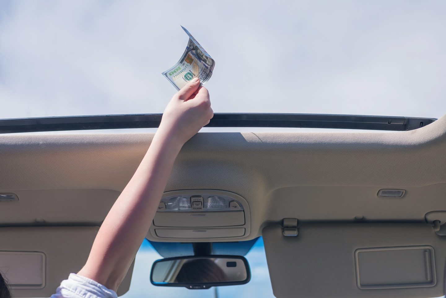 Car passenger holds a $100 bill near the open sunroof