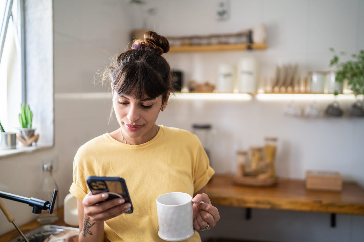 Young woman using the mobile phone while drinking coffee or tea at home